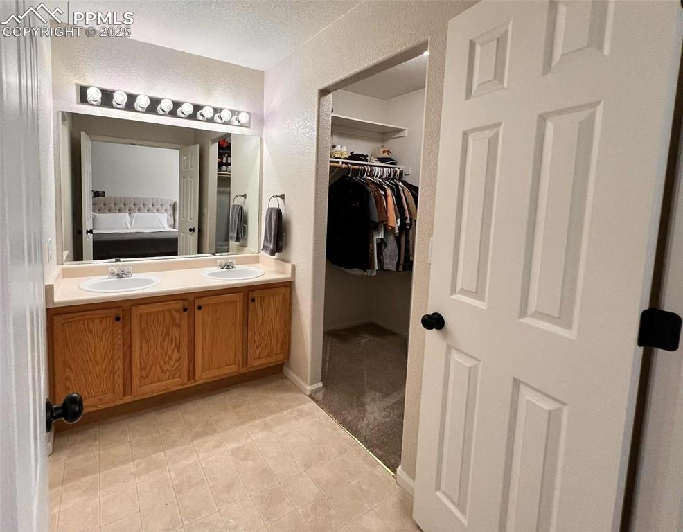 Image 14 of 35: Bathroom featuring a spacious closet, double vanity, a textured wall, and a