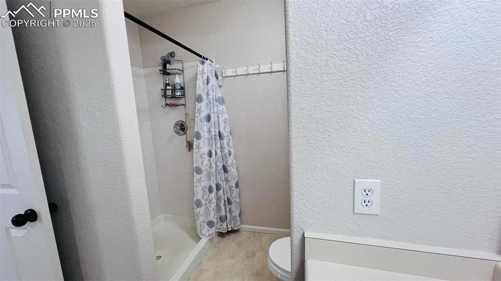 Image 19 of 35: Full bathroom featuring a textured wall, a stall shower, and tile patterned