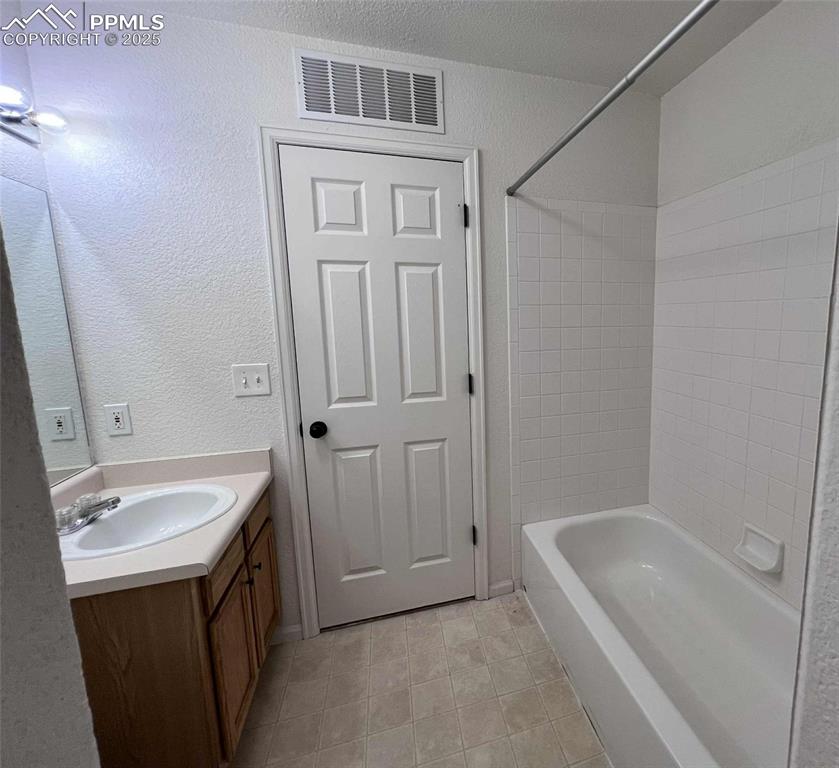 Image 22 of 35: Full bath featuring vanity, a textured wall, tile patterned floors, and sho