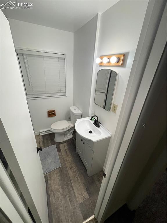 Image 11 of 12: Half bath with wood finished floors, vanity, and baseboard heating