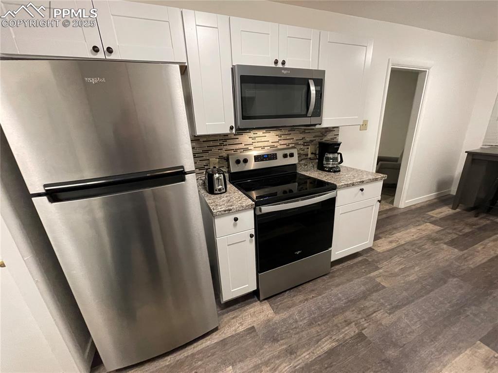 Image 7 of 12: Kitchen featuring stainless steel appliances, white cabinetry, dark wood-st