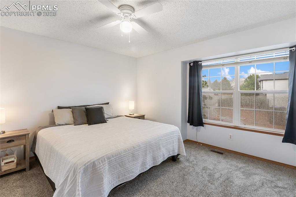 Image 10 of 28: Primary bedroom with carpet, a textured ceiling, and ceiling fan