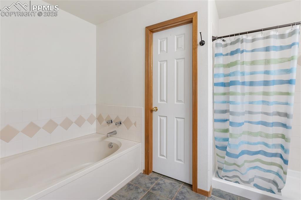 Image 12 of 28: Bathroom featuring a stall shower, a garden tub, and dark tile patterned fl