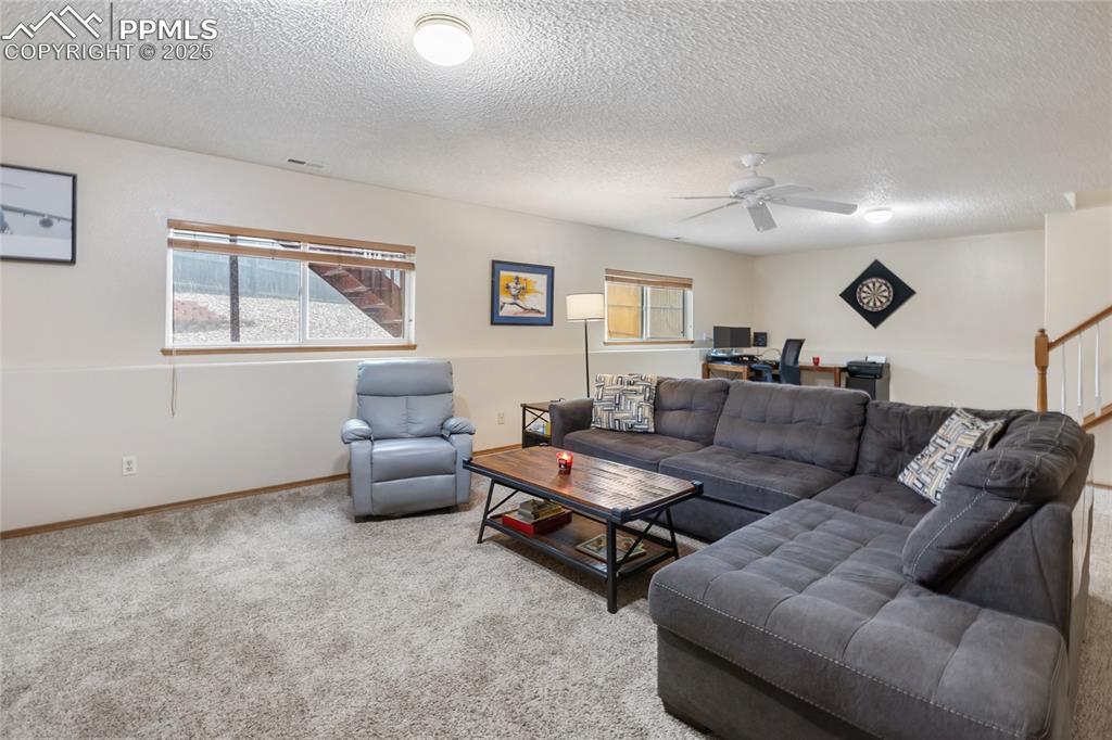 Image 19 of 28: Carpeted living room featuring a textured ceiling, a ceiling fan, and a des