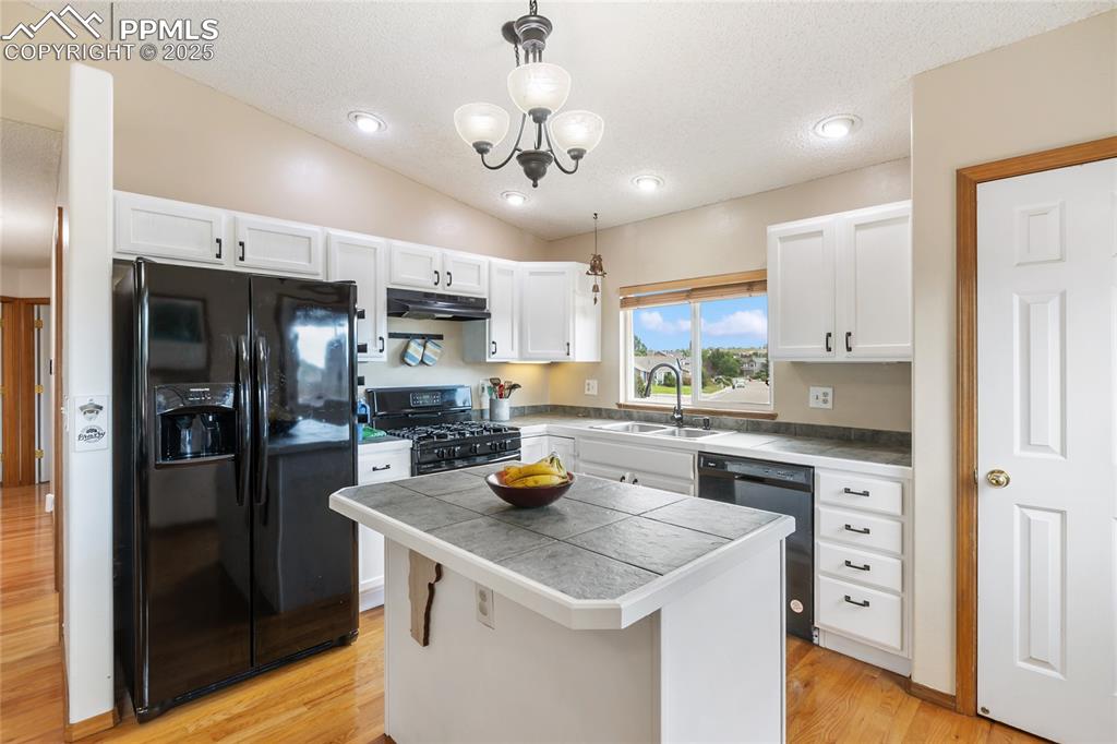 Image 5 of 28: Kitchen with white cabinets, black appliances, pendant lighting, a center i