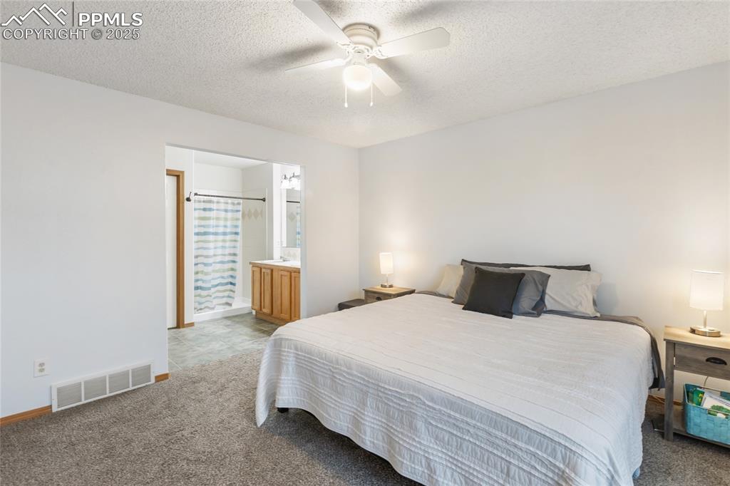 Image 9 of 28: Primary bedroom with carpet floors, ceiling fan, a textured ceiling, and en