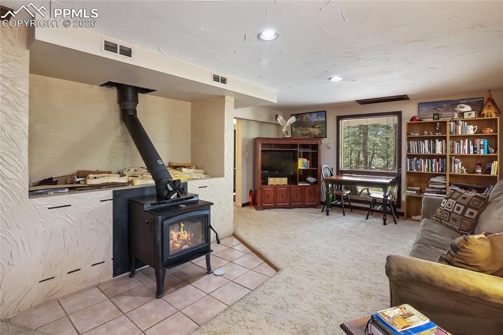 Image 19 of 39: Tiled space in the family room with a wood stove, carpet floors, and recess