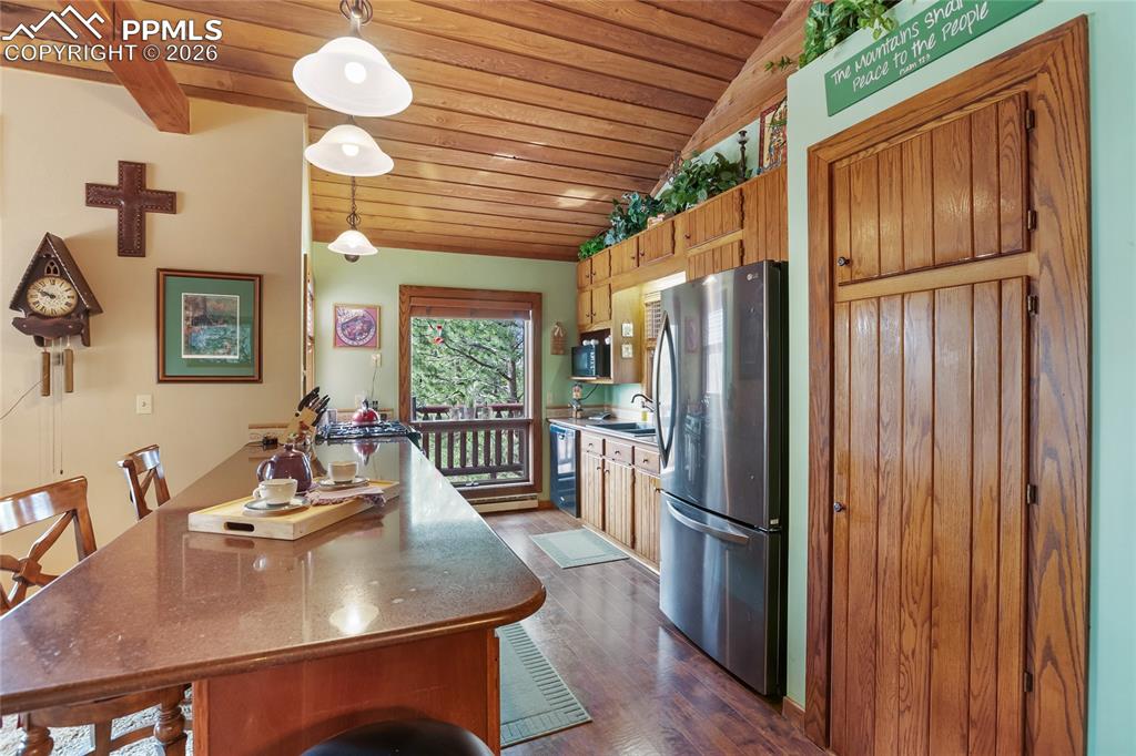 Image 8 of 39: Kitchen with a kitchen bar, wooden lofted ceiling, freestanding refrigerato