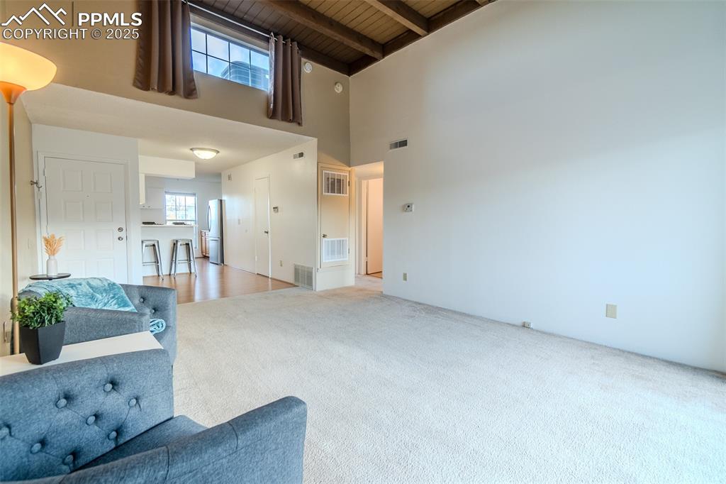 Image 10 of 27: Unfurnished living room with a high ceiling, a wood ceiling with exposed be