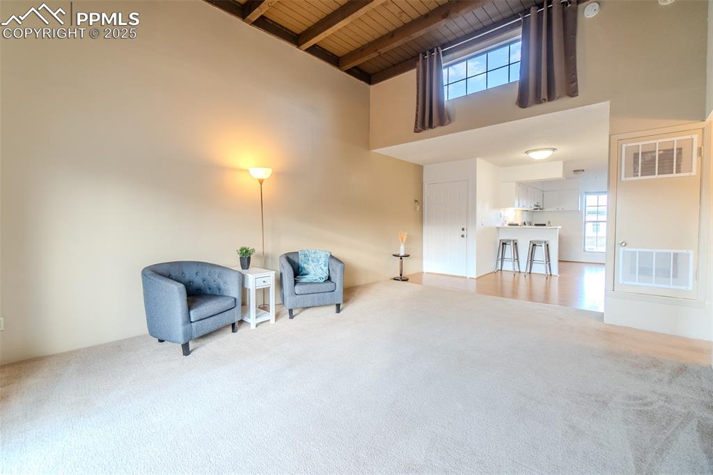 Image 12 of 27: Living area with carpet flooring, a wooden ceiling with exposed beams, and