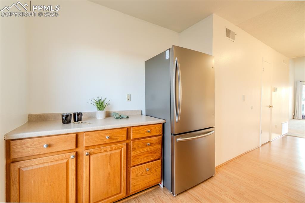 Image 7 of 27: Kitchen with freestanding refrigerator, brown cabinetry, light wood-style f