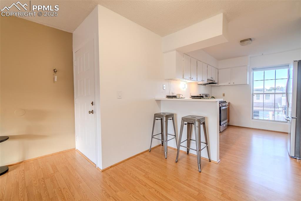 Image 8 of 27: Kitchen featuring a breakfast bar area, white cabinetry, light wood-type fl