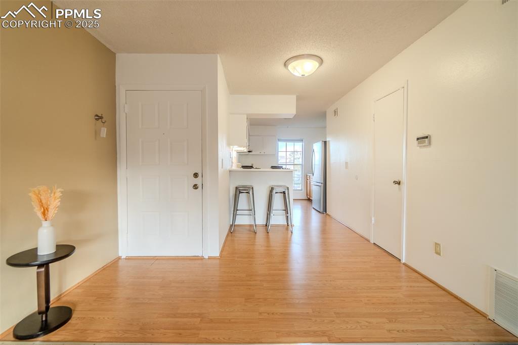 Image 9 of 27: Corridor featuring light wood-type flooring and a textured ceiling