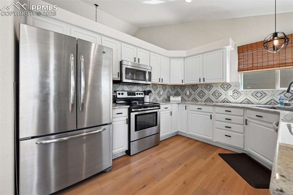 Image 12 of 45: The kitchen features stainless steel appliances, white cabinetry, granite c