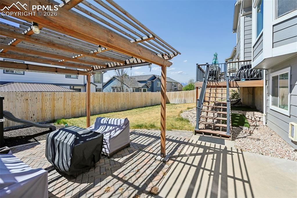 Image 27 of 45: The property features a paved patio area with a wooden pergola, leading to 