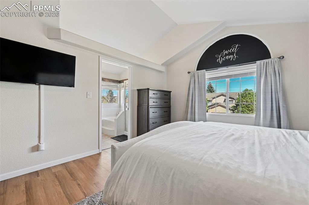 Image 38 of 45: This bedroom features hardwood floors, a vaulted ceiling, and an arched win
