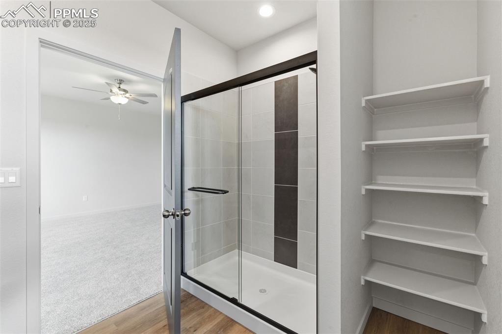 Image 22 of 24: Bathroom featuring a shower stall, ceiling fan, wood finished floors, and c