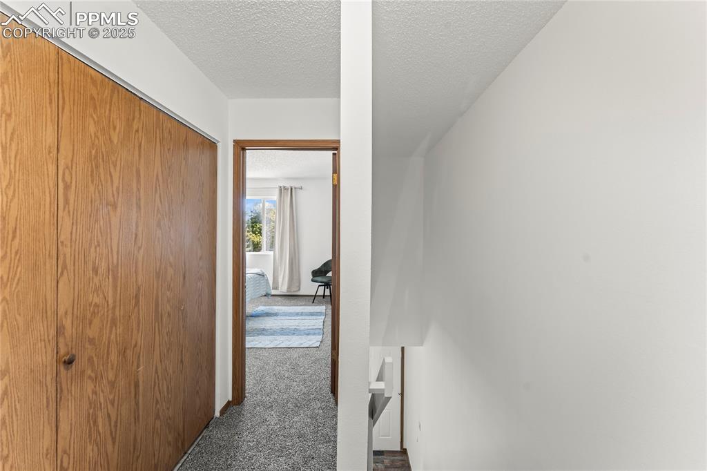 Image 13 of 25: Hall with dark colored carpet and a textured ceiling