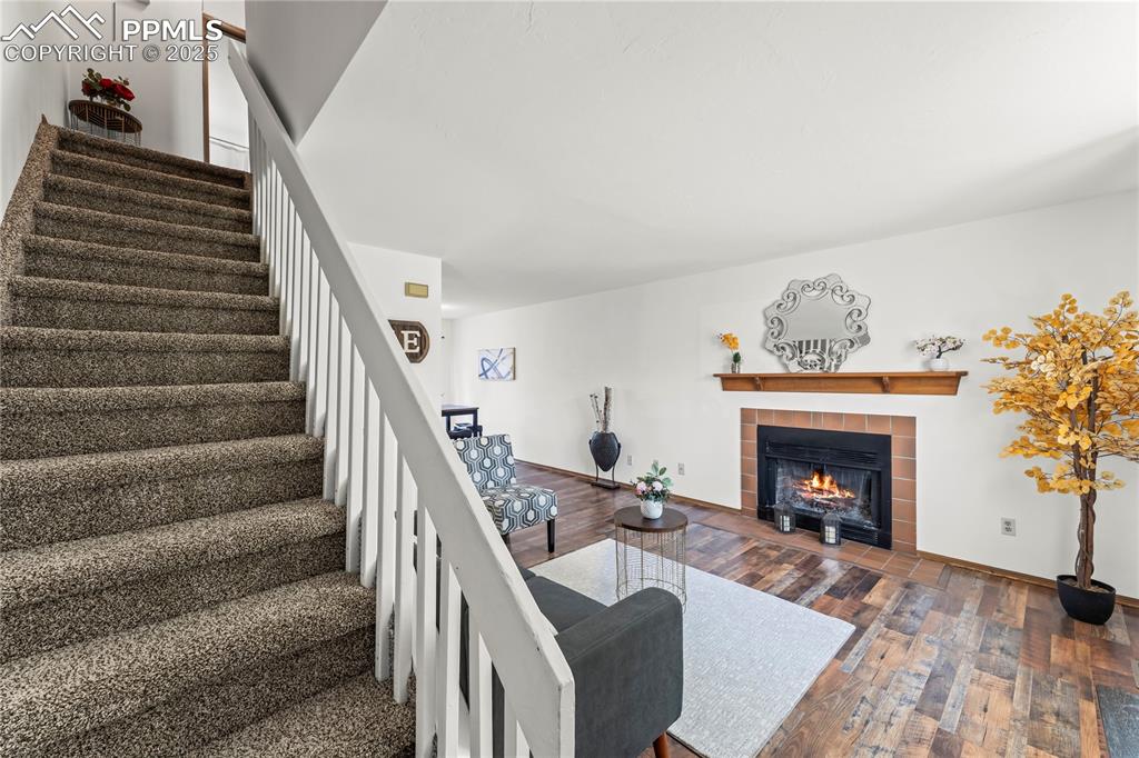 Image 3 of 25: Living area featuring dark wood-style floors, a tiled fireplace, and stairw