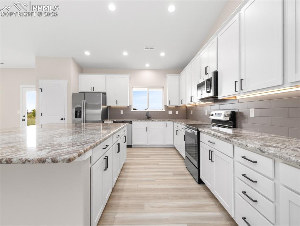 Image 12 of 38: Kitchen with stainless steel appliances, white cabinetry, recessed lighting