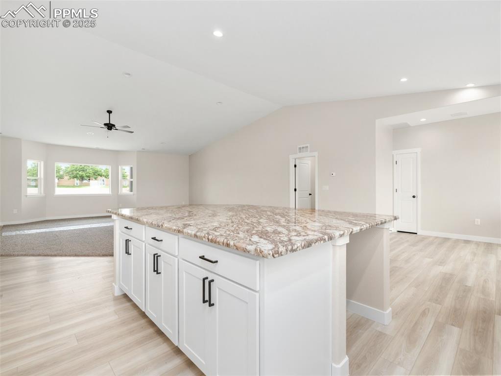 Image 13 of 38: Kitchen with open floor plan, a kitchen island, white cabinetry, light ston