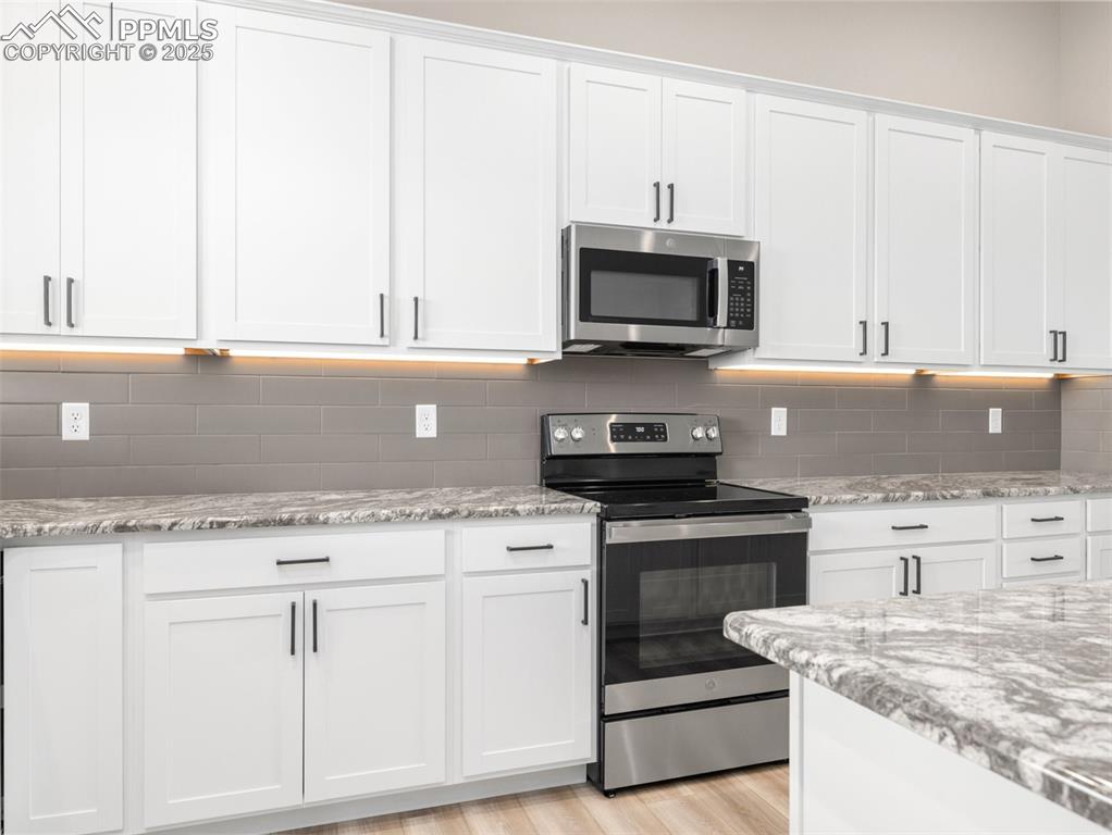 Image 14 of 38: Kitchen with appliances with stainless steel finishes, white cabinetry, lig