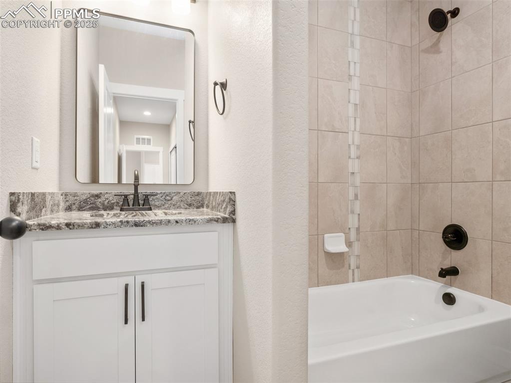 Image 16 of 38: Full bathroom featuring shower / tub combination, vanity, and a textured wa