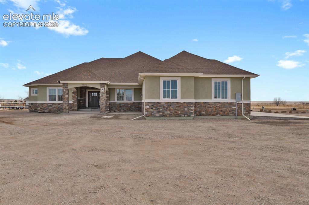 Caption: Stucco exterior with stone accents, covered entry, multiple windows, and a brown shingle roof