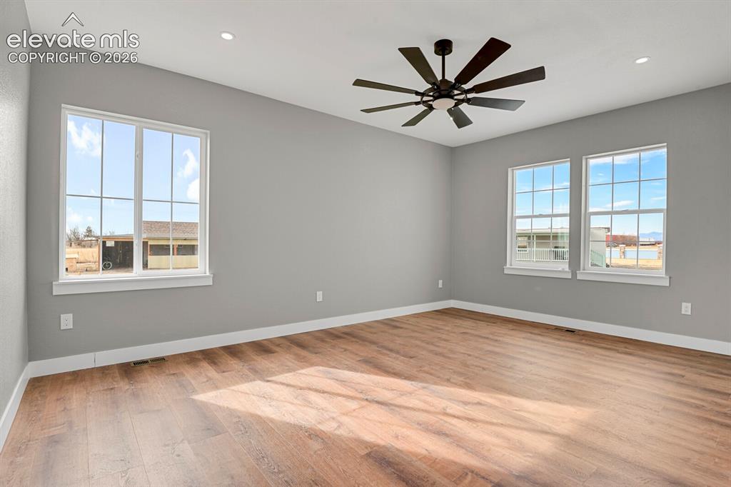 Image 21 of 49: Spacious room featuring wood-finish flooring, multiple windows, a ceiling f