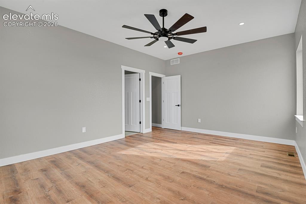 Image 22 of 49: Spacious room with wood-finish flooring, light gray walls, and a contempora