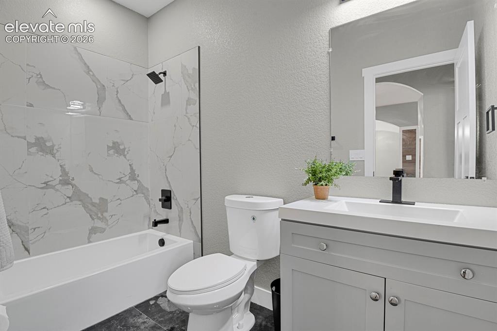 Image 28 of 49: White tub/shower combination with large format marble-look tile surround
