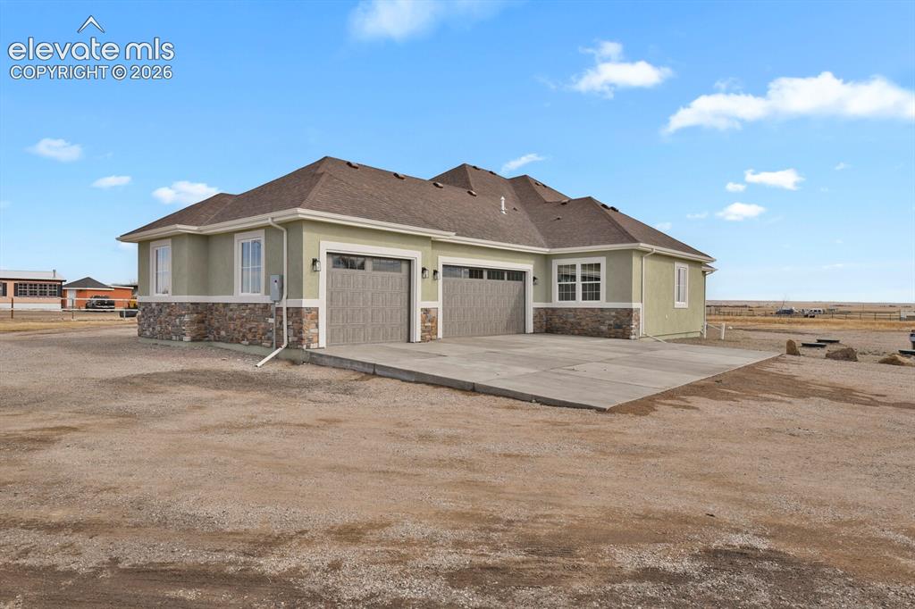 Image 3 of 49: Stucco exterior with a stone veneer accent, multiple garage bays with panel