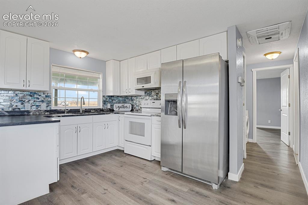 Image 38 of 49: Kitchen featuring white cabinetry, a mosaic tile backsplash, wood-finish fl