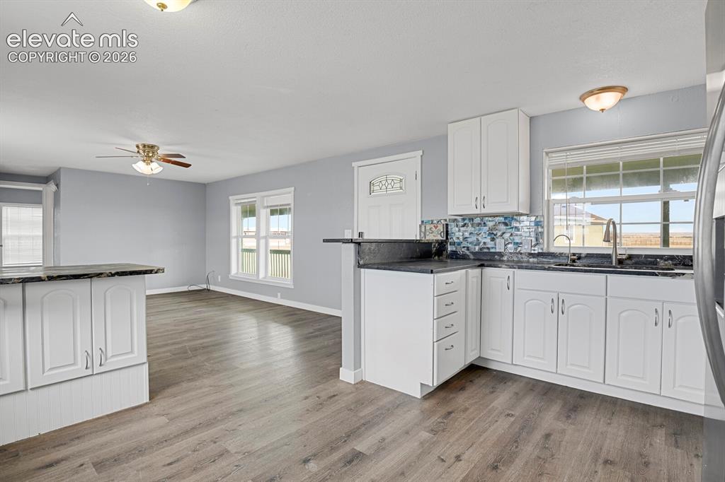 Image 39 of 49: Wood-finish flooring, white cabinetry, dark countertops, a decorative backs