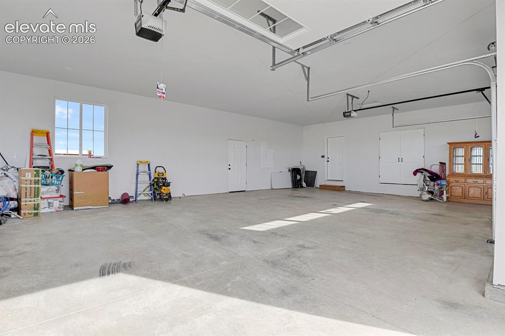 Image 45 of 49: Spacious garage featuring a concrete floor, high ceilings, multiple doors,