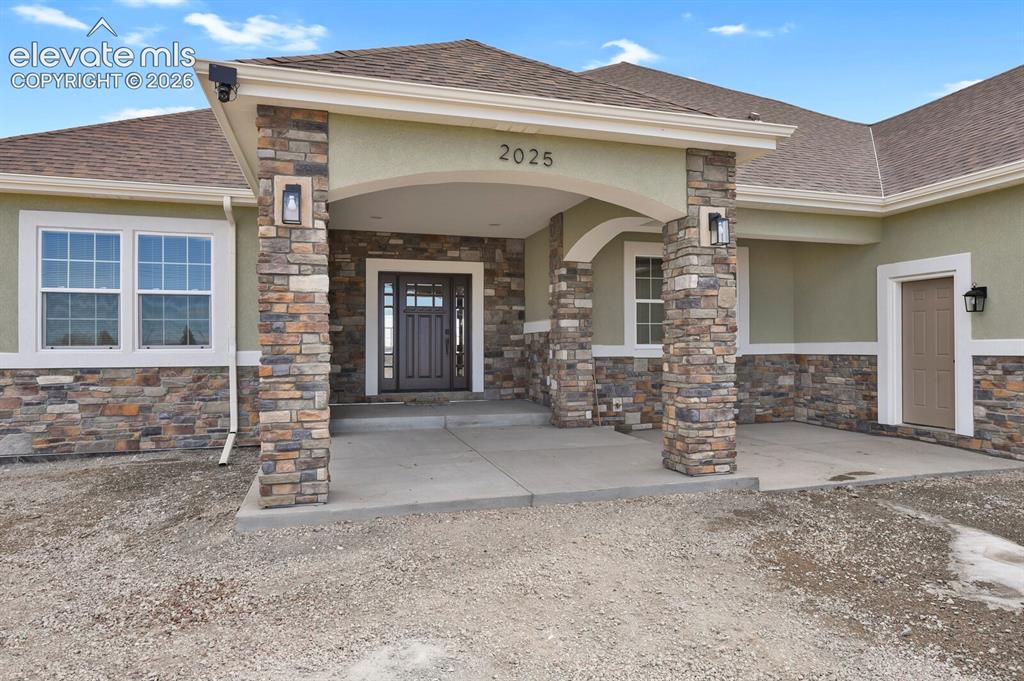 Image 7 of 49: Stone façade entry with a covered porch, arched details, and decorative out