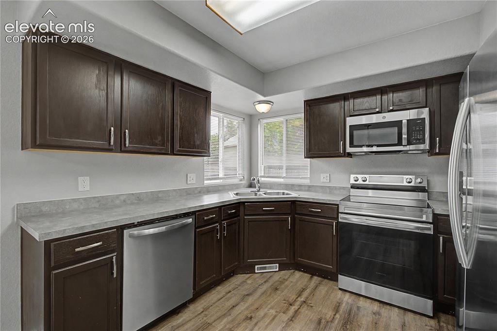 Image 11 of 18: Kitchen featuring wood-finish flooring, dark wood cabinetry, gray counterto