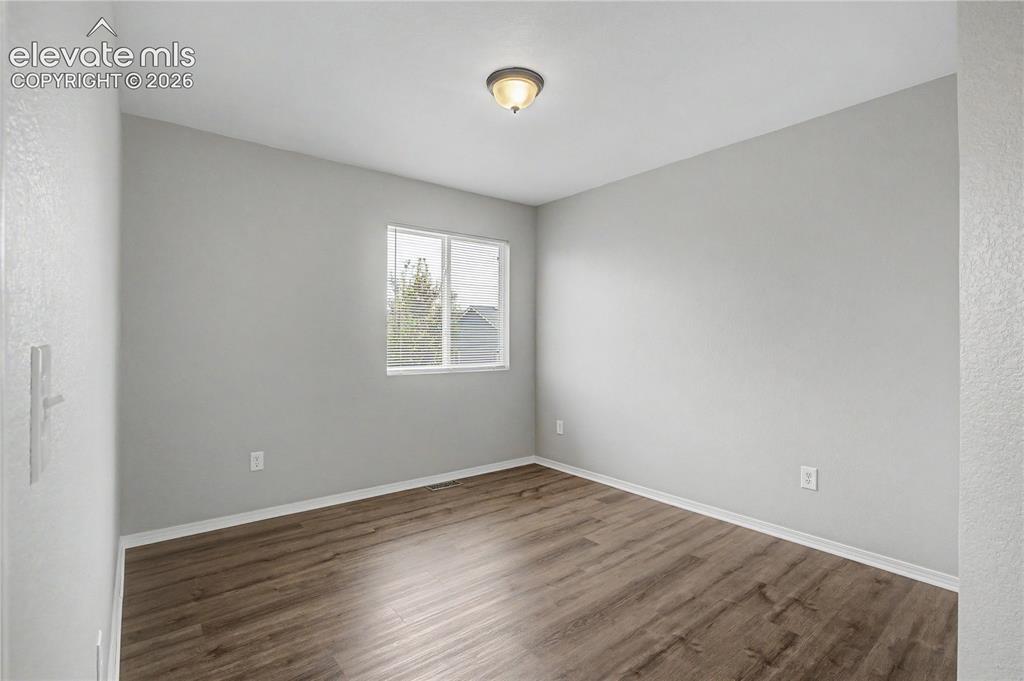 Image 12 of 18: Spacious room featuring wood-finish flooring, light gray walls, white baseb
