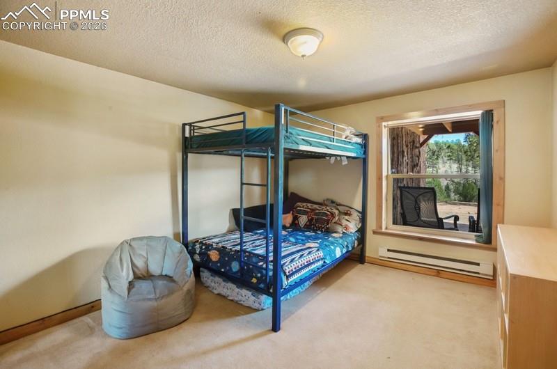 Image 17 of 32: Bedroom featuring a baseboard heating unit, light carpet, a textured ceilin