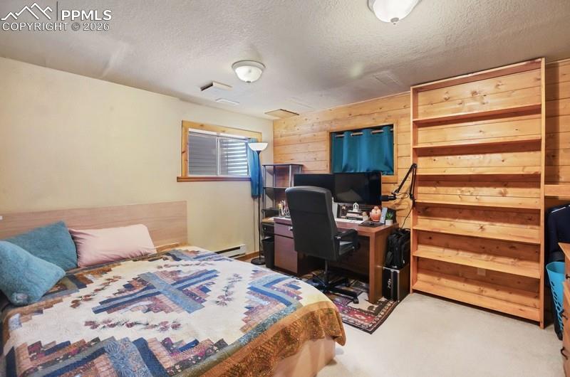 Image 19 of 32: Bedroom featuring wood walls, a baseboard radiator, carpet floors, a textur