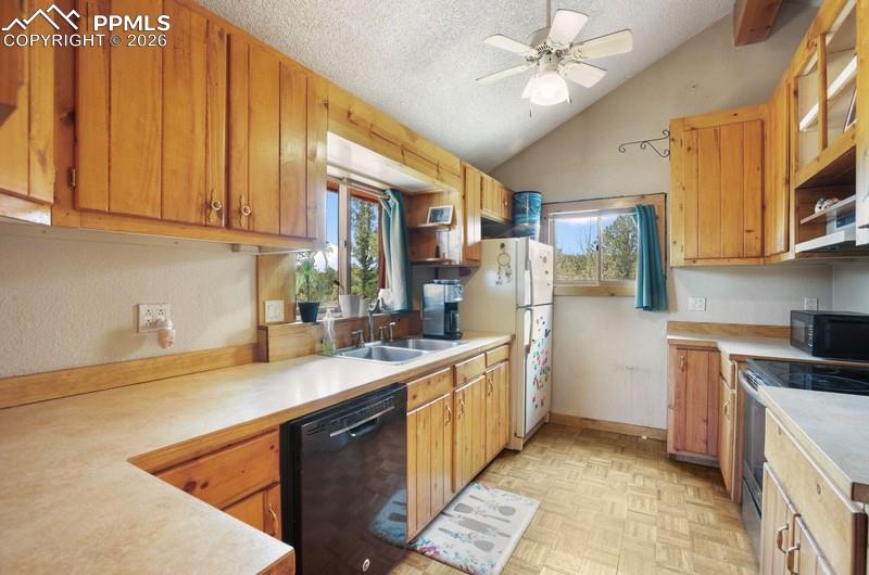 Image 9 of 32: Kitchen featuring black appliances, vaulted ceiling, light countertops, ple