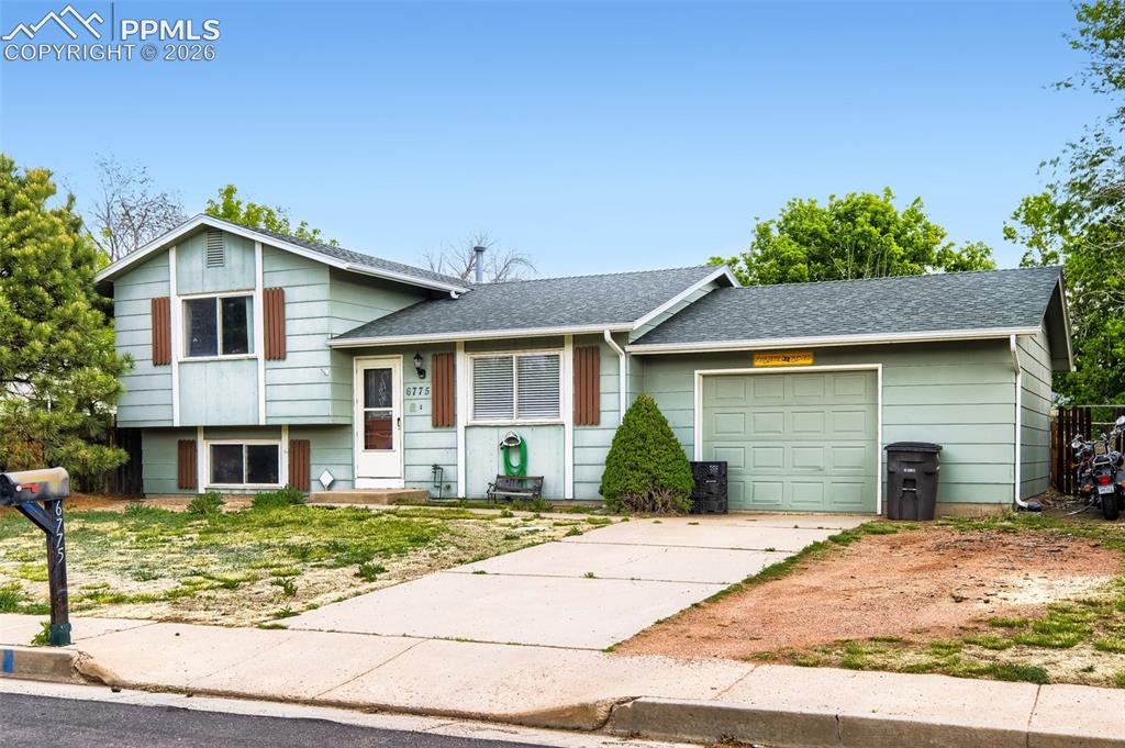 Image 2 of 28: Split-level property featuring light green siding and a dark shingled roof