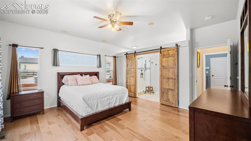 Image 19 of 42: Bedroom with a barn door, light wood-type flooring, and ceiling fan