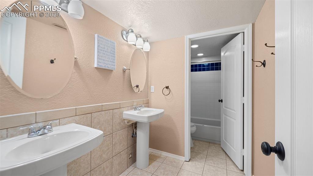 Image 29 of 42: Bathroom featuring two sinks, a textured ceiling, tile walls, shower / tub 