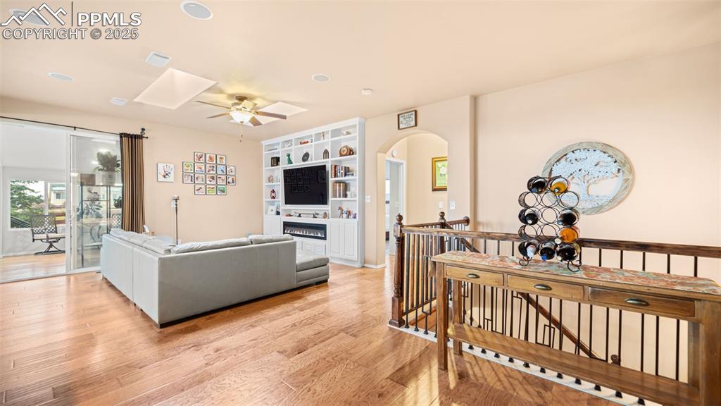 Image 7 of 42: Living area with built in shelves, light wood finished floors, arched walkw