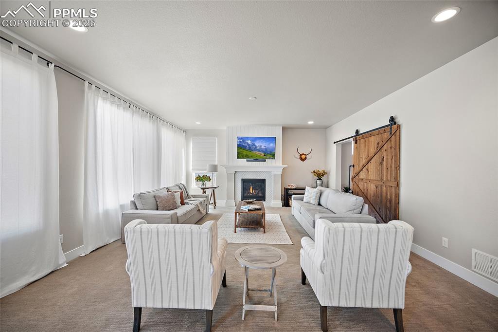 Image 12 of 45: Living room featuring a barn door, carpet floors, a lit fireplace, and rece