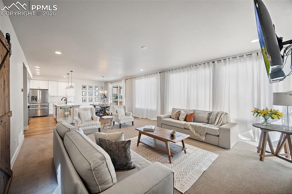 Image 13 of 45: Living area with light carpet, a barn door, and recessed lighting