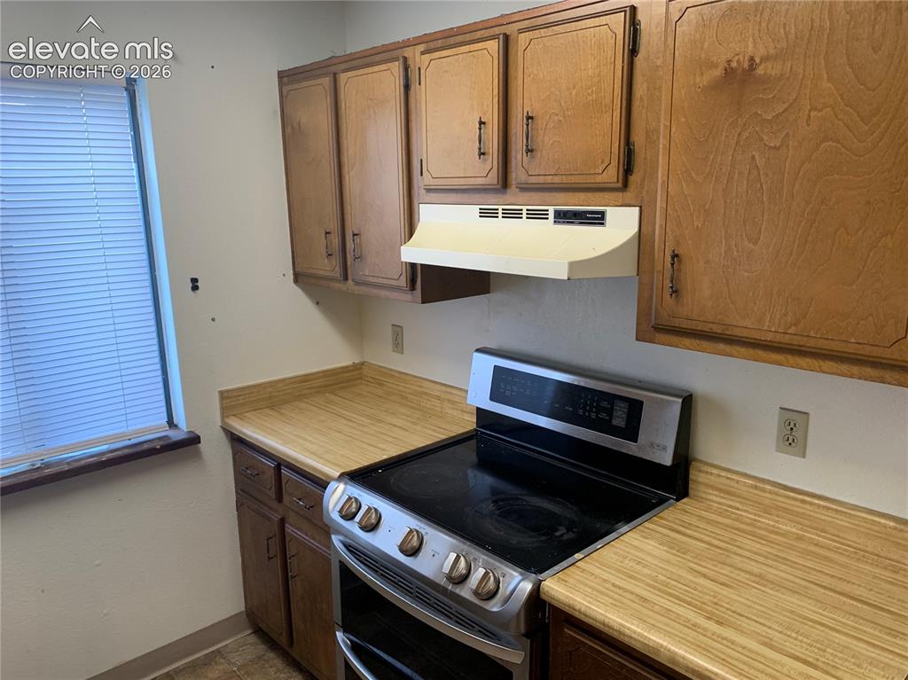 Image 13 of 27: Kitchen area featuring an electric range, range hood, wood-finish cabinetry