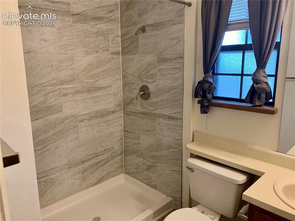 Image 16 of 18: Shower with tile surround, built-in shelving, and a vanity with an integrat