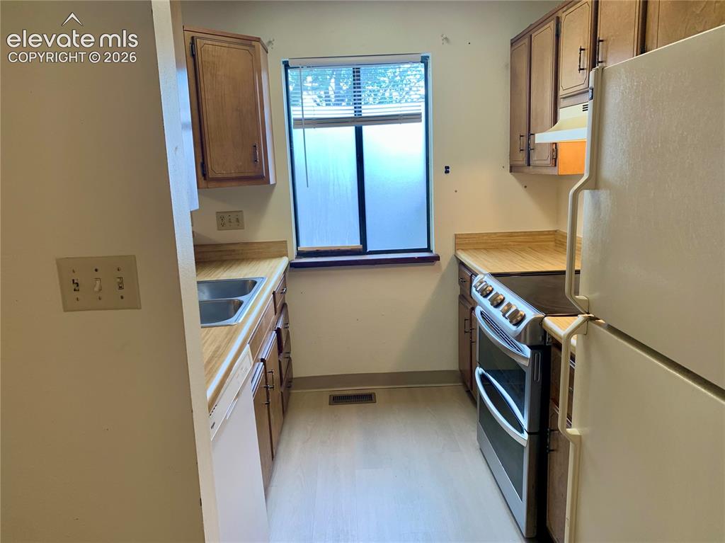 Image 6 of 18: Galley kitchen featuring wood-finish cabinetry, a double basin sink, and a
